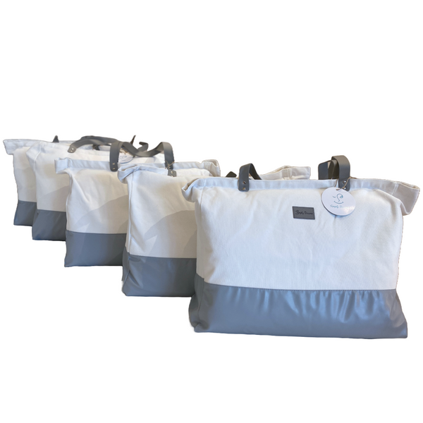 Multiple large canvas and gray fabric tote bags with brown handles lined up, one showing a 'Simply Dreams' tag.