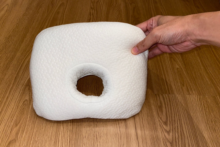 A hand presses into a white baby comfort pillow, demonstrating its soft and breathable latex material, ideal for gentle newborn head support and flat head prevention.